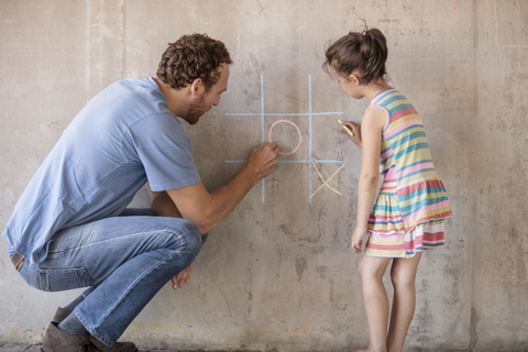 Vater und Tochter spielen Tic-Tac-Toe mit Kreide an einer Betonwand, lizenzfreies Stockfoto