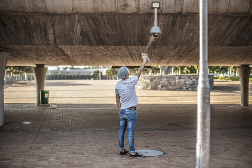 Man wearing a white mask spraing a security camera with spraypaint - ZEF14905