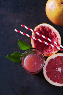 Ganze und in Scheiben geschnittene Pink Grapefruit, Blätter, Strohhalme und ein Glas Grapefruitsaft - CSF28594