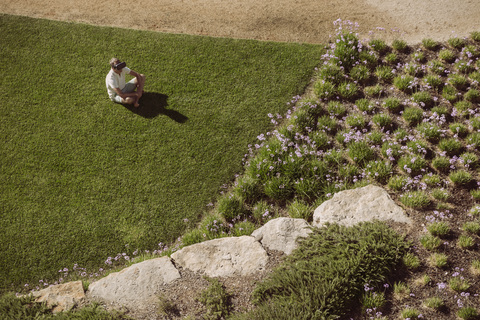 Mann mit VR-Brille sitzt auf Rasen im Garten, lizenzfreies Stockfoto
