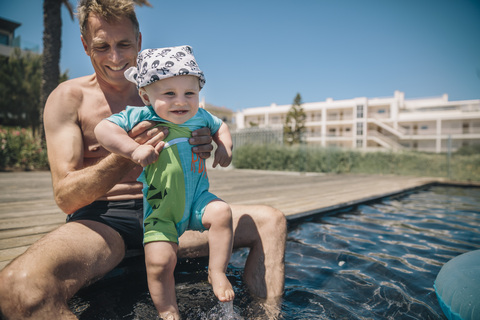 Vater und kleiner Sohn testen Wasser im Schwimmbad während der Sommerferien, lizenzfreies Stockfoto