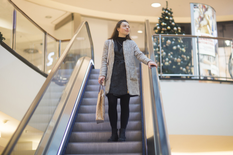 Junge Frau mit Einkaufstasche auf Rolltreppe in einem Einkaufszentrum zur Weihnachtszeit, lizenzfreies Stockfoto