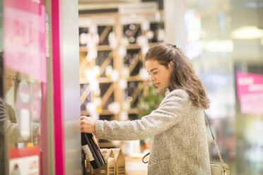 Junge Frau wählt im Supermarkt eine Flasche Rotwein aus - SGF02125