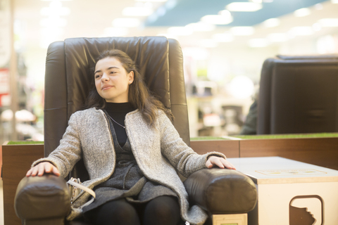 Porträt einer selbstbewussten jungen Frau, die sich in einem Ledersessel in einem Geschäft ausruht, lizenzfreies Stockfoto