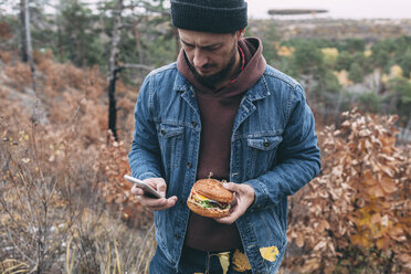 Mann mit Burger und Smartphone - VPIF00294