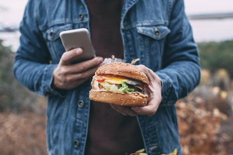 Mann mit Burger und Smartphone, lizenzfreies Stockfoto