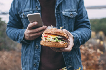 Mann mit Burger und Smartphone - VPIF00295