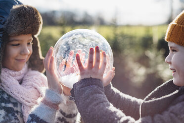 Bruder und Schwester schauen in eine mit Schnee gefüllte Kristallkugel und wünschen sich etwas - MJF02211