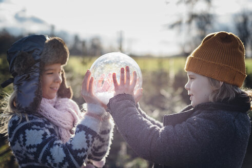 Brother and sister looking into crystal ball filled with snow, making a wish - MJF02212