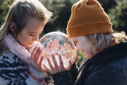 Brother and sister looking into crystal ball filled with snow, making a wish - MJF02214
