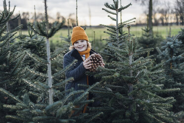 Little boy standing among fir trees, holding pine cone - MJF02222