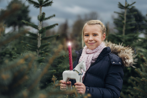 Little girl standing in front of fir trees with a burning candle stock photo