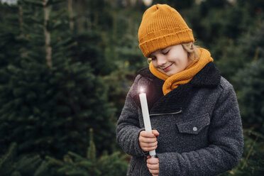 Little boy standing in front of fir trees with a burning candle - MJF02231