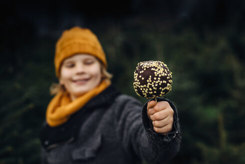 Kleiner Junge steht vor einer Tanne und hält einen in Schokolade getauchten Apfel - MJF02242