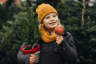 Fröhlicher Junge bereitet sich auf Weihnachten vor, hält einen Topfbaum und isst einen in Schokolade getauchten Apfel - MJF02248