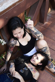 Tätowiertes lesbisches Paar, das lacht und Spaß auf einer Holzbrücke hat - IGGF00255