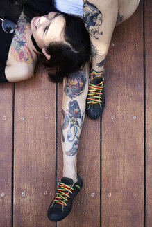 Happy woman lying on leg of tattooed girl friend on planks - IGGF00256