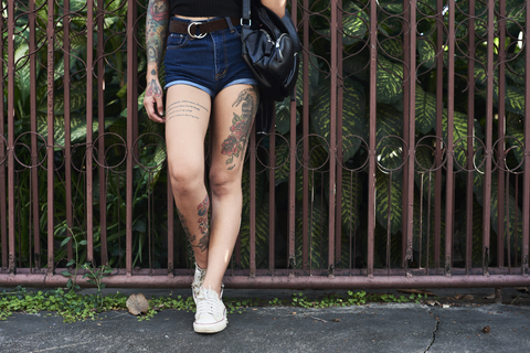 Legs of tattooed woman standing at garden fence stock photo