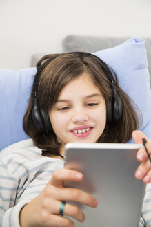 Porträt eines lächelnden Mädchens, das zu Hause ein Tablet und Kopfhörer benutzt - LVF06509