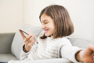 Porträt eines lachenden Mädchens mit Kopfhörern und Smartphone auf der Couch - LVF06511