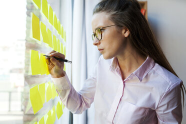 Geschäftsfrau schreibt auf Post it an Glasscheibe - VABF01444