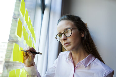 Businesswoman writing on post it at glass pane - VABF01445