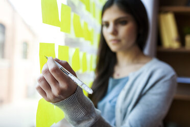 Businesswoman writing on post it at glass pane - VABF01446