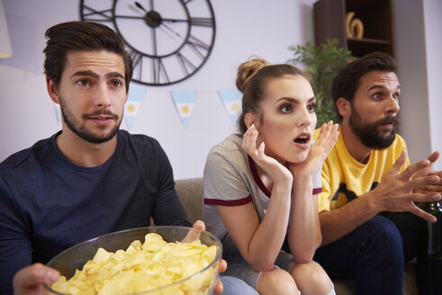 Aufgeregte Freunde, die auf dem Sofa sitzen und fernsehen - ABIF00089