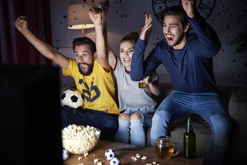 Excited friends sitting on the sofa watching Tv - ABIF00094