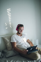 Smiling young man relaxing at home with his tablet - RAEF01951