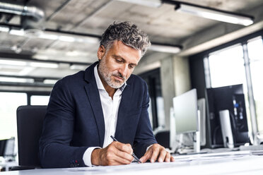 Mature businessman writing at desk in office - HAPF02524