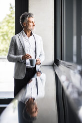 Smiling mature businessman with coffee mug looking out of window - HAPF02546