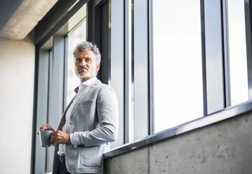 Mature businessman with coffee mug at the window - HAPF02547