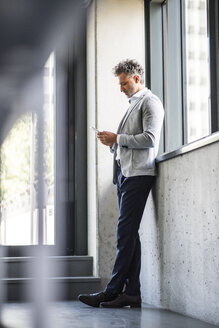 Reifer Geschäftsmann, der am Fenster steht und ein Mobiltelefon hält - HAPF02551