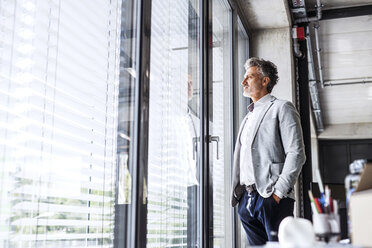 Reifer Geschäftsmann im Büro stehend und aus dem Fenster blickend - HAPF02556