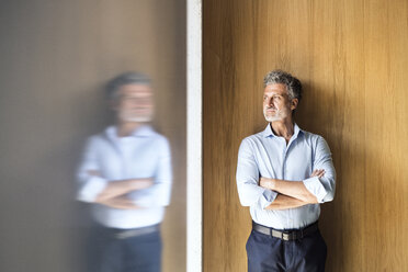 Reflection of mature businessman standing at wooden wall - HAPF02569