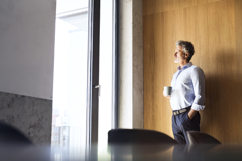 Mature businessman with coffee mug looking out of window stock photo