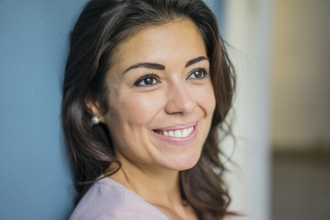 Porträt einer glücklichen jungen Frau, die sich an eine Wand lehnt, lizenzfreies Stockfoto