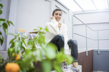 Porträt einer glücklichen jungen Frau, die auf einer Terrasse sitzt - MOEF00447