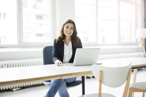 Porträt einer glücklichen Geschäftsfrau, die am Schreibtisch im Büro sitzt und am Laptop arbeitet, lizenzfreies Stockfoto