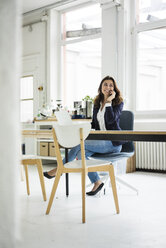 Porträt einer lachenden Geschäftsfrau am Telefon, die an einem Schreibtisch in einem Loft sitzt - MOEF00454