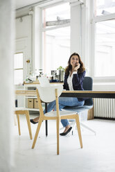 Portrait of laughing businesswoman on the phone sitting at desk in a loft - MOEF00454