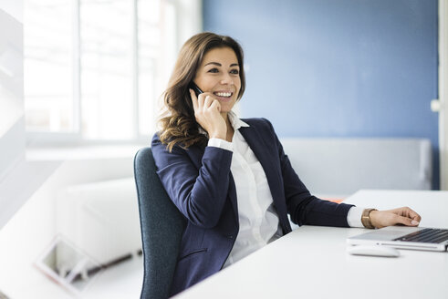 Porträt einer lächelnden Geschäftsfrau am Telefon, die an einem Schreibtisch in einem Büro sitzt - MOEF00455