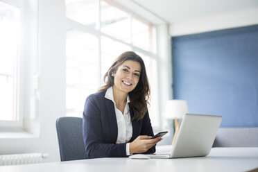 Portrait of happy businesswoman sitting at desk in the office - MOEF00458
