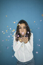 Portrait of young woman blowing confetti in the air - MOEF00474