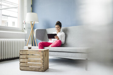 Smiling woman sitting on couch using tablet - MOEF00476