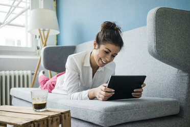 Portrait of laughing woman relaxing on couch with tablet - MOEF00478