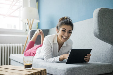 Porträt einer lachenden Frau, die sich mit einem Tablet auf der Couch entspannt - MOEF00479