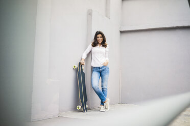 Smiling young woman with skateboard leaning against wall on terrace - MOEF00483