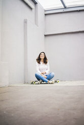 Lächelnde junge Frau sitzt auf einem Skateboard auf einer Terrasse - MOEF00484